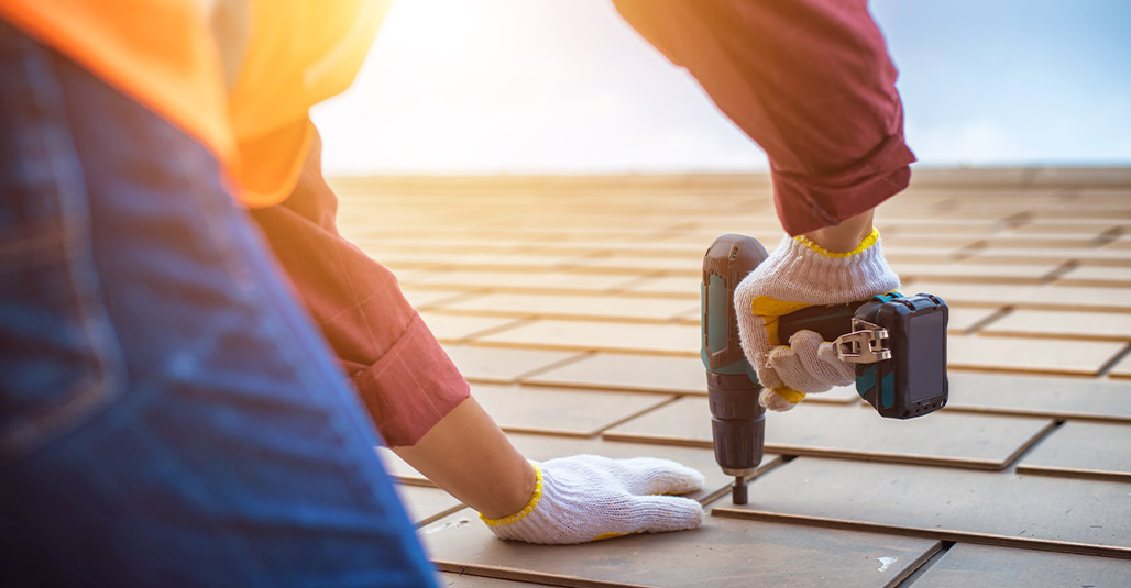 A person using a drill to secure roofing materials as part of storm-proofing their home before an impending storm.