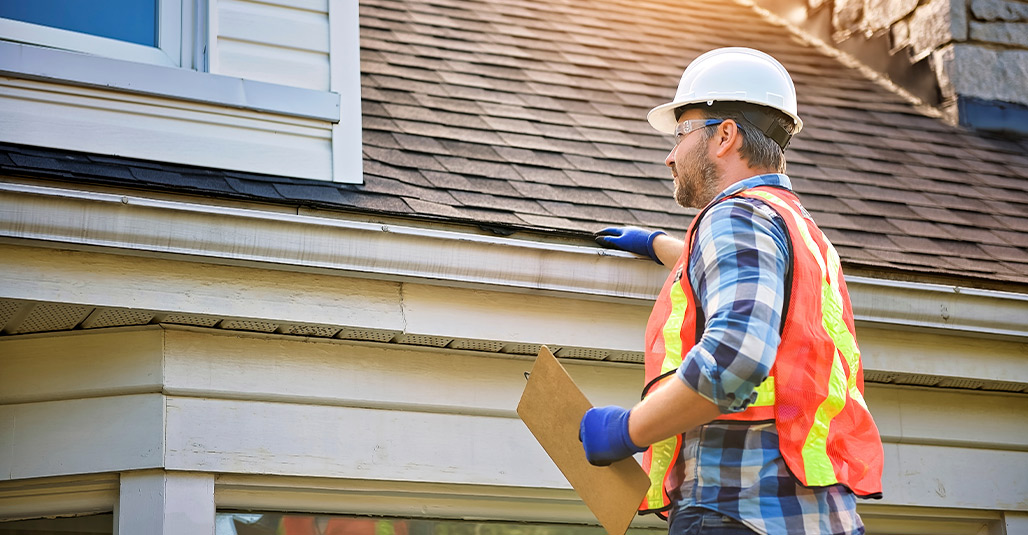 A man wearing a hard hat and safety vest stands with a clipboard, ready to discuss storm-proofing strategies for homes.