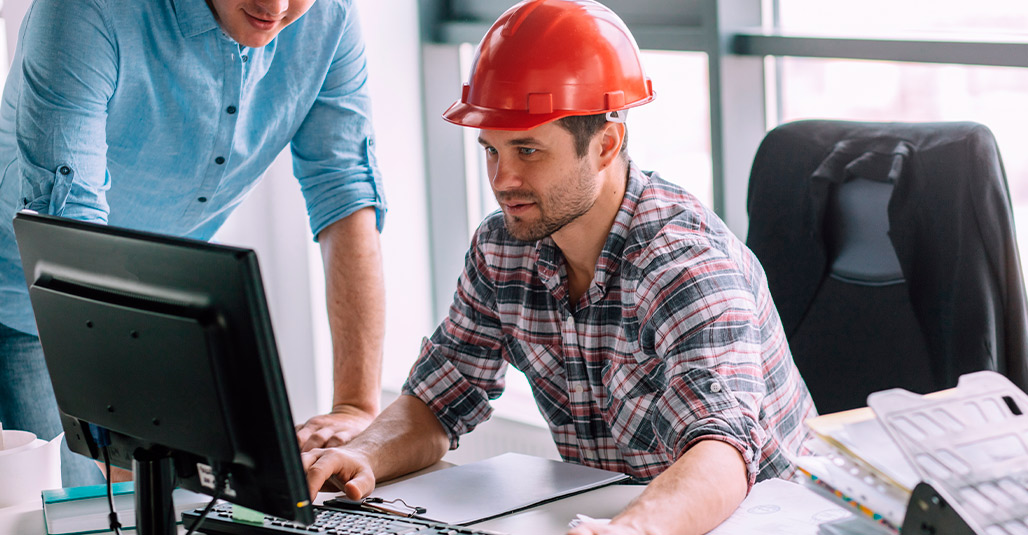 Two men wearing hard hats work together on a computer, focused on custom home building projects in McAllen.