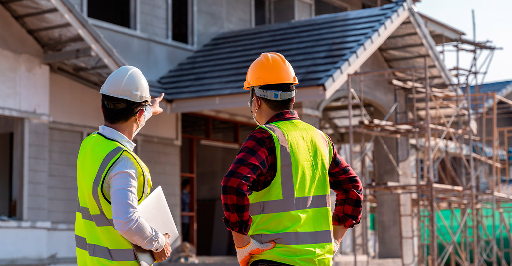 Two construction workers pose in front of a house, ready to build custom homes in McAllen.