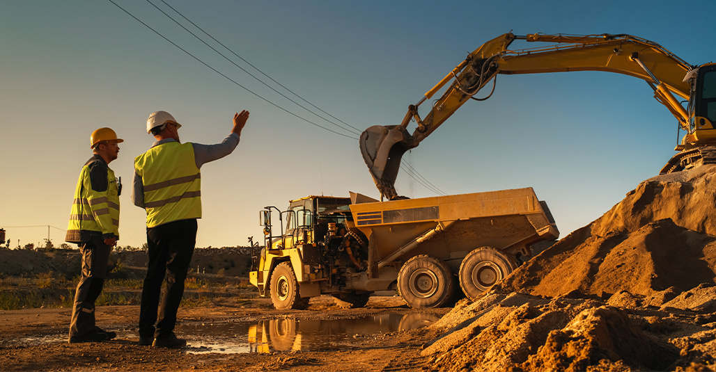 Two men wearing yellow vests are next to a dump truck, representing the commercial construction industry in South Texas.