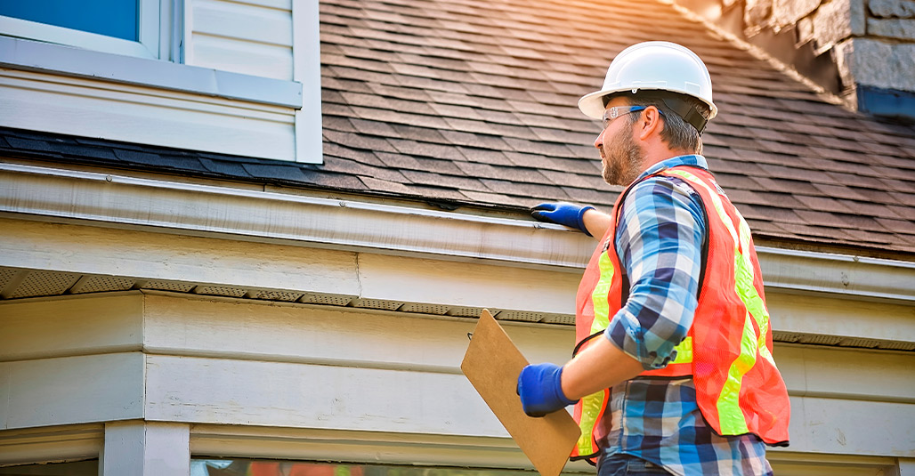 A man wearing a safety vest and hard hat stands with a clipboard, focused on preparing homes for cooler weather in South Texas.