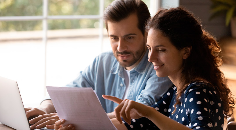 A man and woman examine a document on a laptop, focusing on the advantages and disadvantages of building or buying in McAllen.