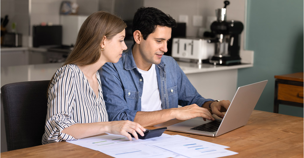 A man and woman sit at a table with a laptop, discussing their new home budget in McAllen.