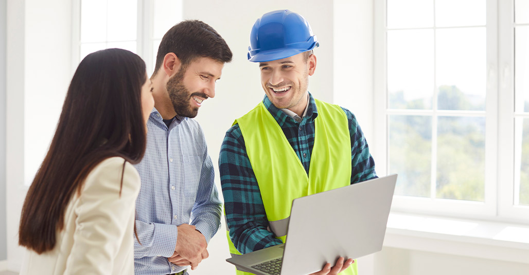 Two men and a woman in hard hats and safety vests review a laptop, discussing a new home budget in McAllen.